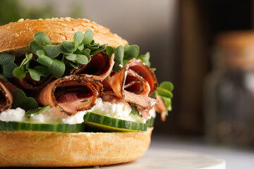 A bagel sandwich with pastrami, cucumber slices, watercress salad and ricotta on marble background, close-up, selective focus