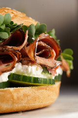 A bagel sandwich with pastrami, cucumber slices, watercress salad and ricotta on marble background,...