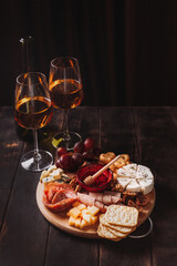 Sausage and cheese cut on round board with fruit, cookies and sauce with two glasses of white port and a bottle