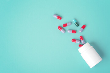 Spilled pills with white medicine bottle on green background