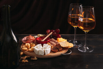 Sausage and cheese cut on round board with fruit, cookies and sauce with two glasses of white port and a bottle