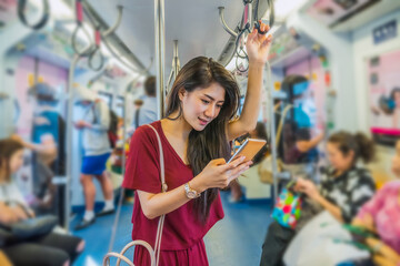 Asian woman passenger with casual suit using the smart mobile phone in the BTS Skytrain rails or...