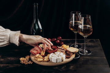 Woman's hand takes crackers from the Appetizers board with assorted cheese, meat, sausage rosette, grape and cookies.