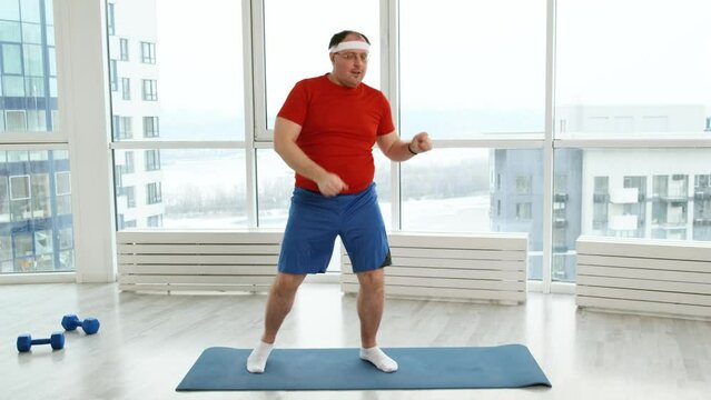 Funny overweight man in red T-shirt dancing in light studio. Happy cheerful fat nerdy man dancing and having fun