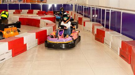 a the smiling little girl in a helmet in the go-kart on the karting track indoors