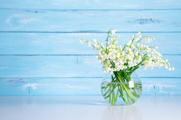 Lily of the valley flowers in glass vase with shadow on wooden blue background.