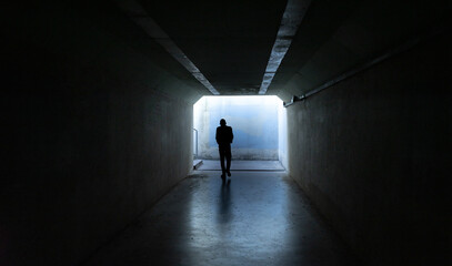 Person walking in dark tunnel exit, front view