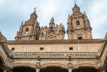 Fototapeta na wymiar Parte alta del patio de estilo gótico de la casa de las conchas y sobresaliendo las torres barrocas de la iglesia La Clerencia en Salamanca, España