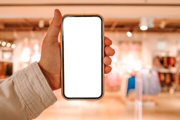 A girl holds a phone in her hand with a blank isolated screen on the background of a blurred shopping center