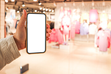 A girl holds a phone in her hand with a blank isolated screen on the background of a blurred shopping center