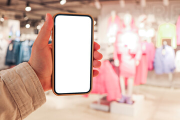 A girl holds a phone in her hand with a blank isolated screen on the background of a blurred shopping center