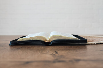 Open Holy Bible on a old wooden table and white wall background. Religion concept.