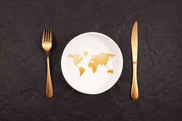Bread in shape world map on white plate. Gold fork and knife on a dark stone background. Abstract...