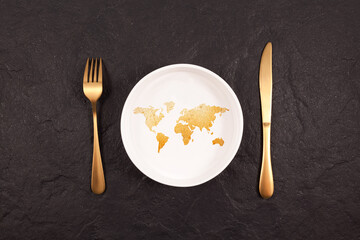 Bread in shape world map on white plate. Gold fork and knife on a dark stone background. Abstract Concept of global hunger