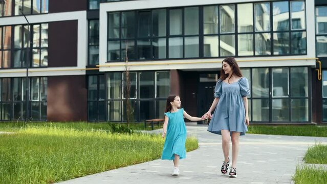 Young mother with her little daughter having a walk near living buildings