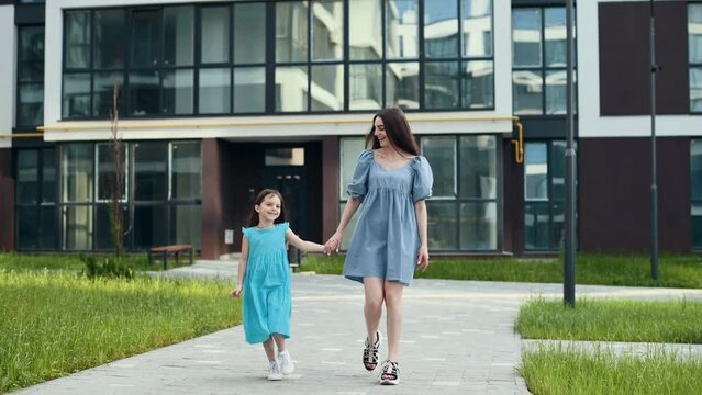 Young mother with her little daughter having a walk near living buildings