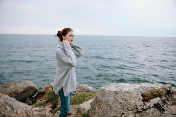 woman in a gray sweater stands on a rocky shore nature Relaxation concept