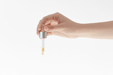 female hand holds a pipette with oil or cosmetic product on a white background