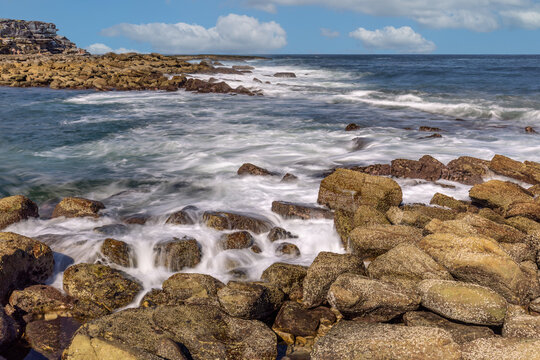 Long exposure shot of waves breaking on the rocks at Clovelly Beach, Randwick, Sydney, Australia, with blue sky and clouds over the horizon.