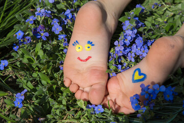 on children's bare feet, lying among flowers, smiling face and a heart are drawn in yellow and blue. Children against war. attracting attention of world community to problem of Ukraine