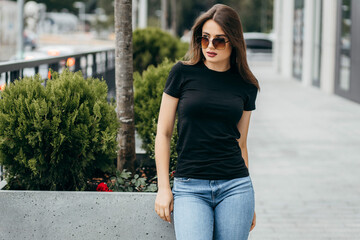 Stylish brunette girl wearing black t-shirt and glasses posing against street , urban clothing style. Street photography	
