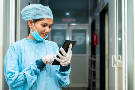 Happy surgeon busy using digital tablet at hospital corridor outside operation theater after surgery - concept of healthcare, technology and relaxation.