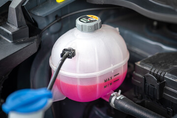 A car's engine coolant water supply box filled with pink color antifreeze liquid. Transportation...