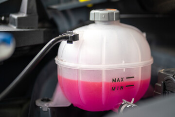 A car's engine coolant water supply box filled with pink color antifreeze liquid. Transportation equipment object photo. - obrazy, fototapety, plakaty
