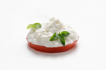 Stracciatella cheese on white background with basil on piece of tomato. Curd cheese product.