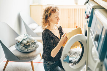 Happy woman housewife in the laundry room near the washing machine with dirty clothes