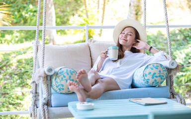 Portrait image of a young woman with hat drinking coffee while relaxing and laying down on swing...