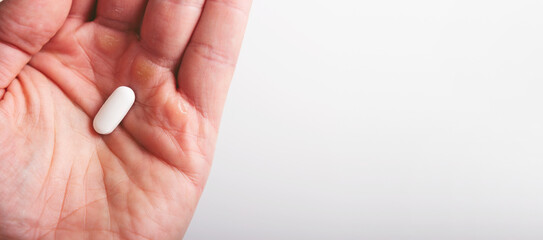 A man holds a white pill in the palm of his hand, close-up