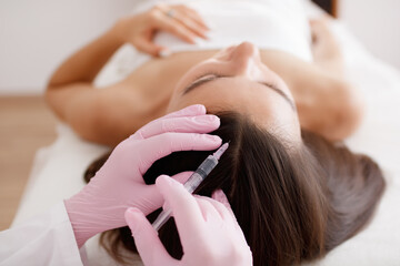 Young woman receiving hair mesotherapy injections from a professional trichologist. Doctor's hands in pink gloves. hair treatment in cosmetology using mesotherapy. injection to the head