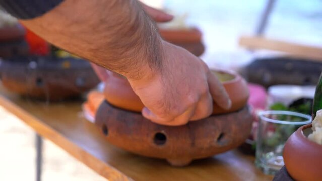 Armenian traditional dish Khash in clay plate. The man's hand puts the boiling khash on the table. Khash in bowl on table․ Traditional dish in Caucasus and Transcaucasia. 