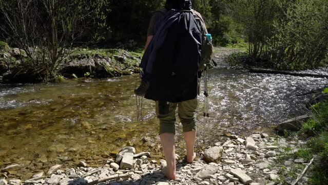 A barefoot mountaineer crosses the river - (4K)
