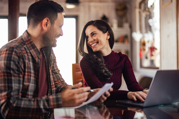 The smiling business couple, working from home, using a laptop and holding some documents.