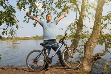 Naklejka premium Happy adult man with bicycle near the river, active recreation concept.