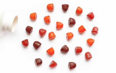 Group of red, orange and purple multivitamin gummies with the bottle isolated on white background. 