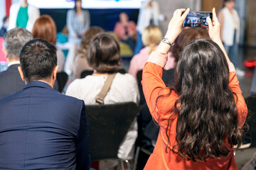 Business conference or corporate presentation, female participant photographing and filming event with a smartphone