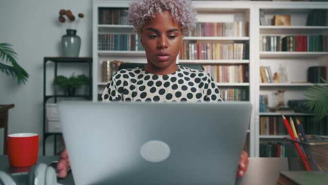 Young attractive African American woman entrepreneur finishes presentation and closes laptop assuming lotus position for meditation and yoga sits at office desk. Businesslady, career, success