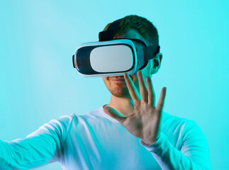 Modern young man experiencing virtual reality glasses in futuristic neon illuminated studio