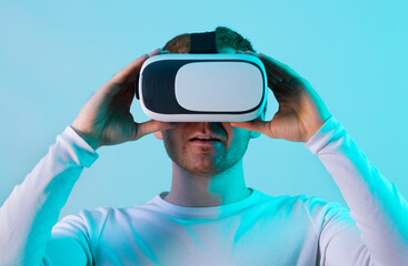 Modern young man experiencing virtual reality glasses in futuristic neon illuminated studio