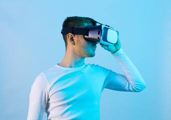 Modern young man experiencing virtual reality glasses in futuristic neon illuminated studio