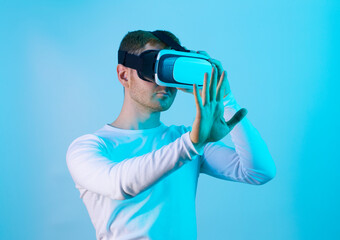 Modern young man experiencing virtual reality glasses in futuristic neon illuminated studio