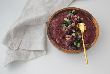 purple smoothie bowl in a wooden bowl decorated with berries, herbs and nuts