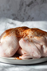 Raw whole chicken seasoned with paprika on a plate. On a marble background