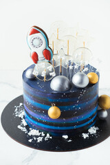 Space themed birthday cake with blue cream cheese frosting decorated with gingerbread cookies in...