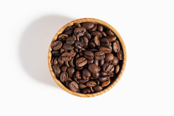 Wooden bowl filled with roasted coffee beans. Coffee beans in bowl isolated on white background. View top.