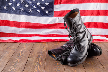 a pair of black police ankle boots stand in front of US flag on wooden surface.