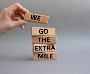 We go the extra mile symbol. Wooden blocks with words 'We go the extra mile'. Beautiful grey background. Businessman hand. Business and 'We go the extra mile' concept. Copy space. - obrazy, fototapety, plakaty